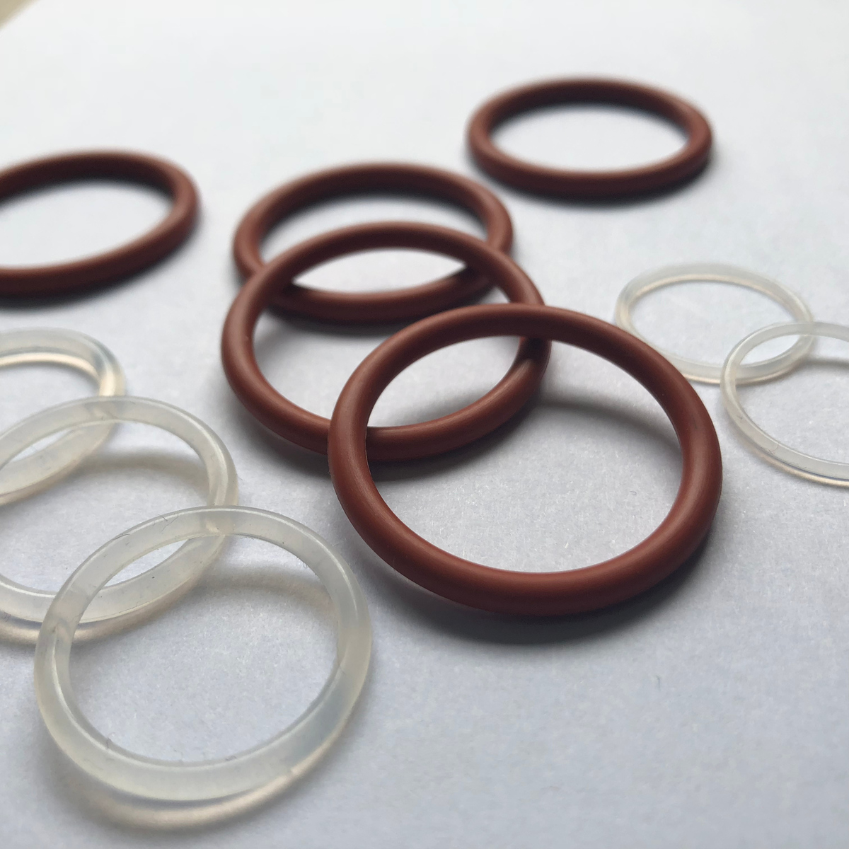 Red-brown and translucent VMQ silicone O-rings arranged on a light background